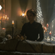 Alicent stands in shadow above the wrapped corpse of Viserys, lying in bed with his crown resting atop him.